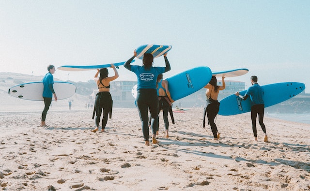 People with surf boards running on the beach